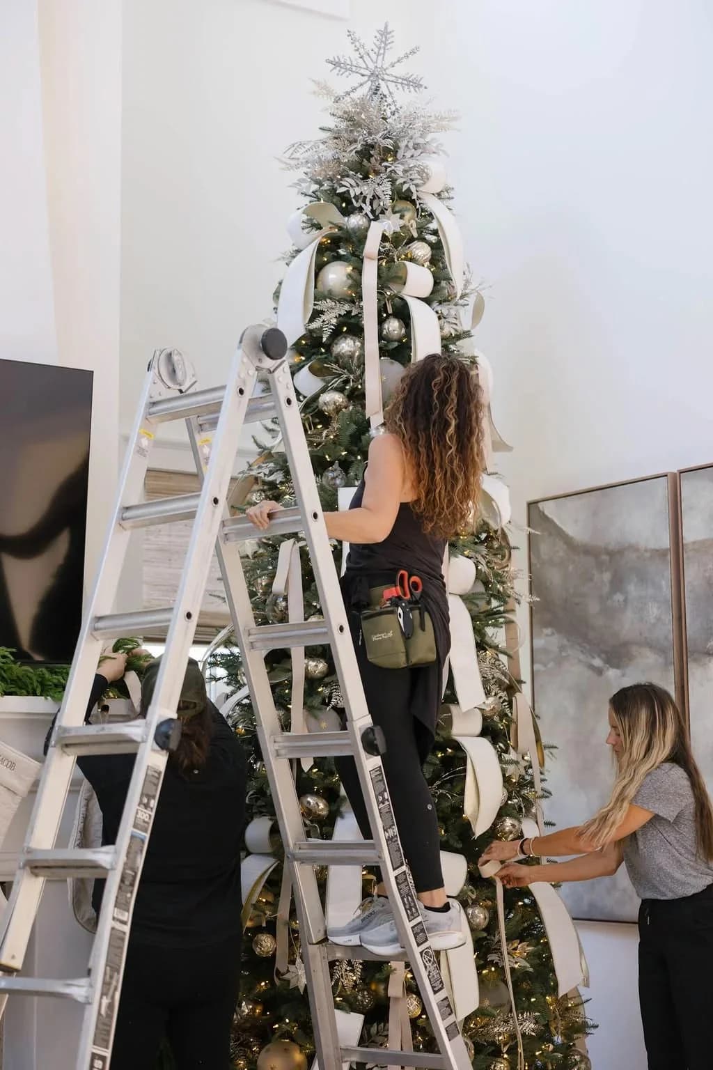 Two people arranging a Christmas tree with a ladder