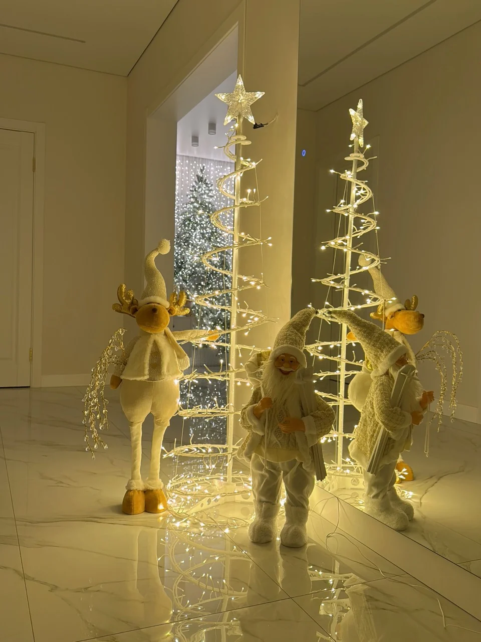 Two star-topped spiral light trees beside Santa and reindeer decorations reflected on a polished floor.