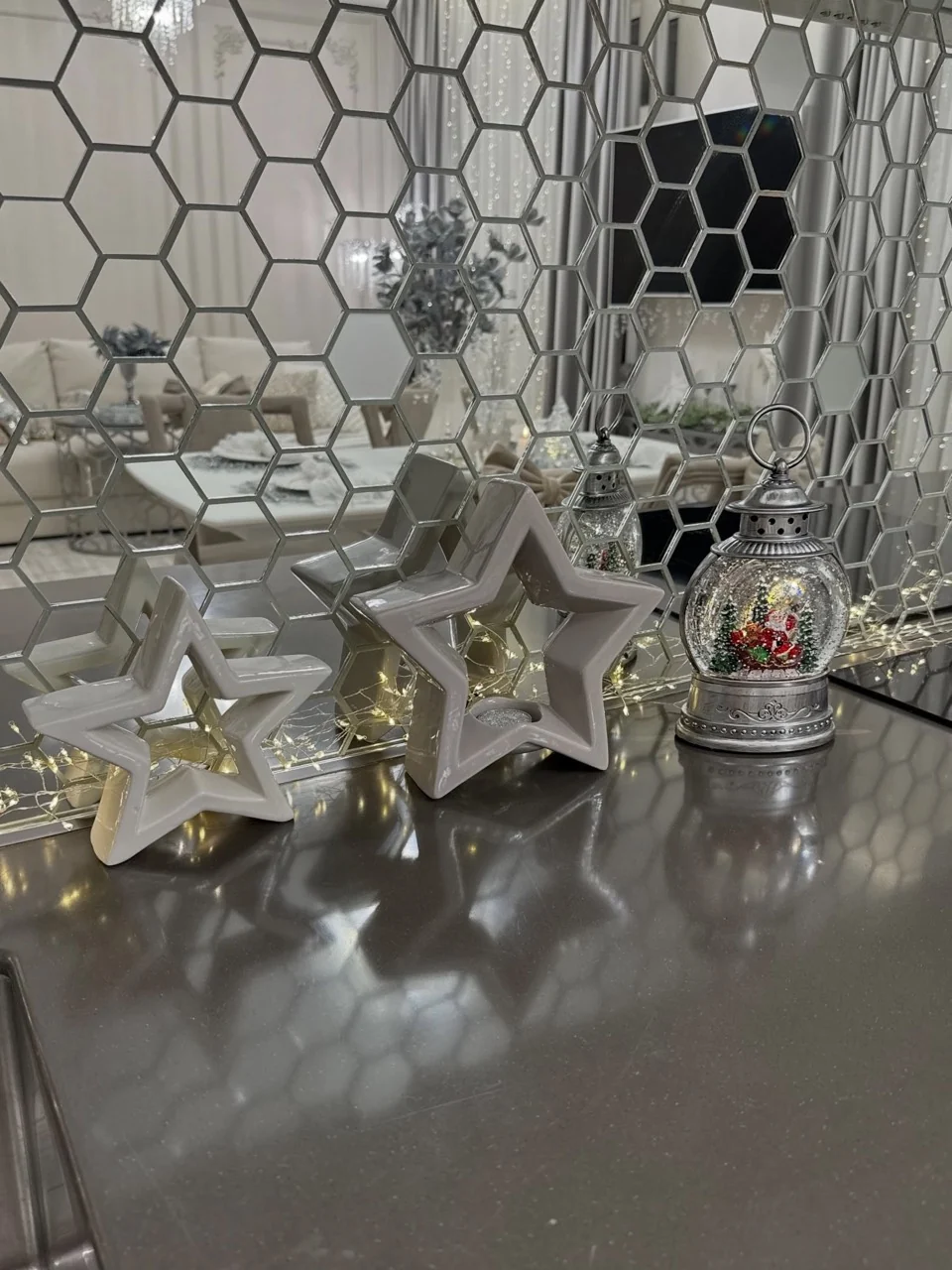 White star decorations, fairy lights and a silver snow-globe lantern on a counter in front of a mirrored tile wall.