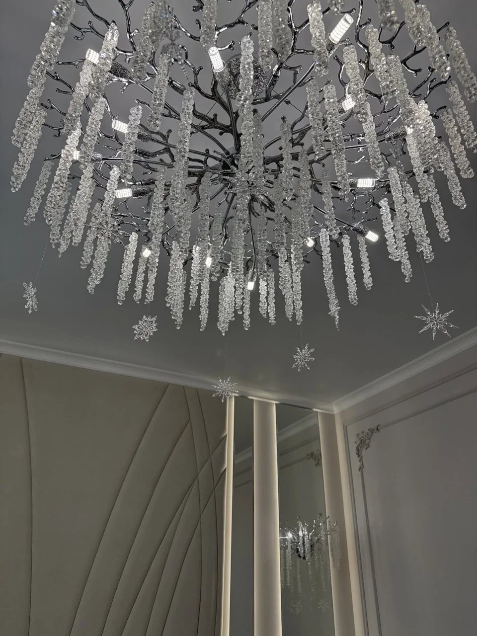 Crystal chandelier with hanging snowflake decorations above a grey and white bedroom.