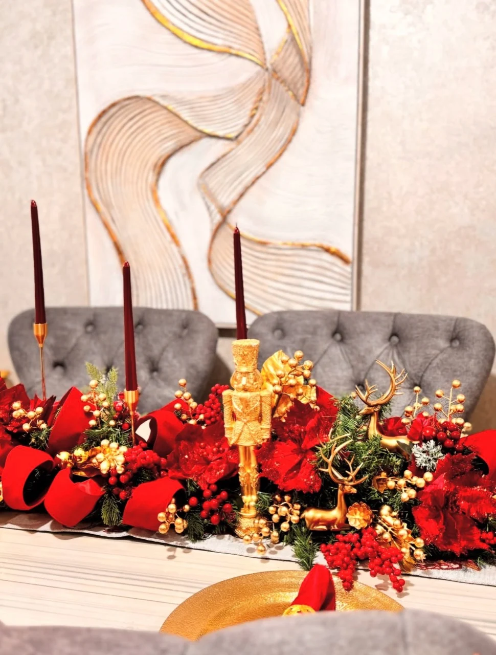 Christmas centerpiece with a gold nutcracker, small gold reindeer, red ribbon, berries and tall red candles.