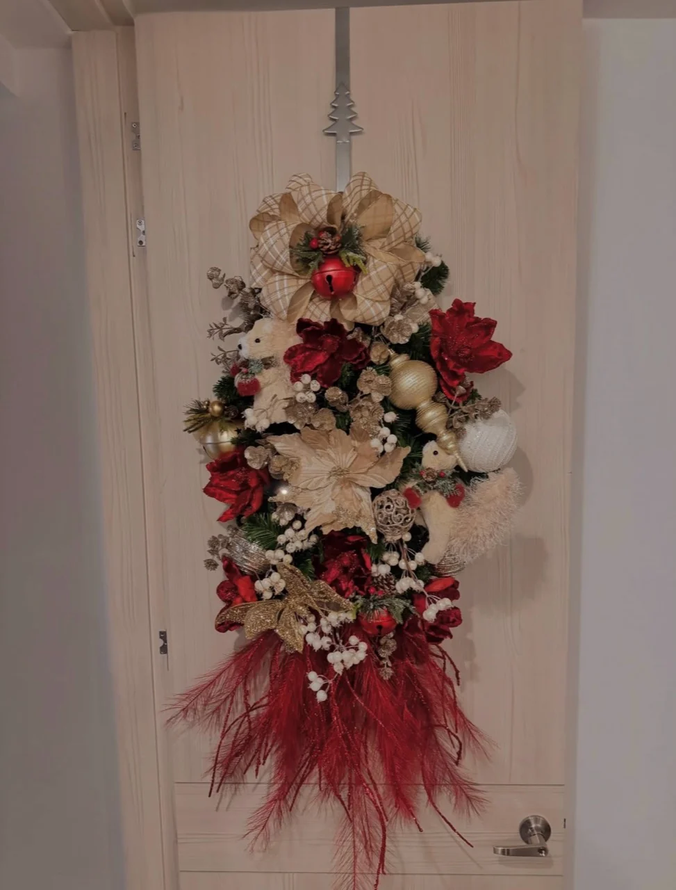 Christmas door swag with a gold plaid bow, red and gold flowers, white berries and trailing red feather-like stems.