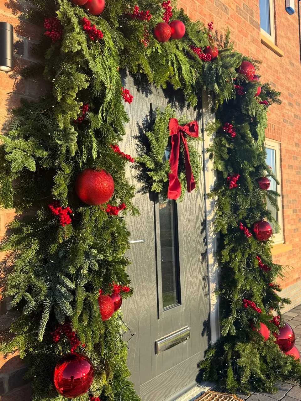 Angled close view of red baubles and berry clusters woven through a thick evergreen garland around a front door.