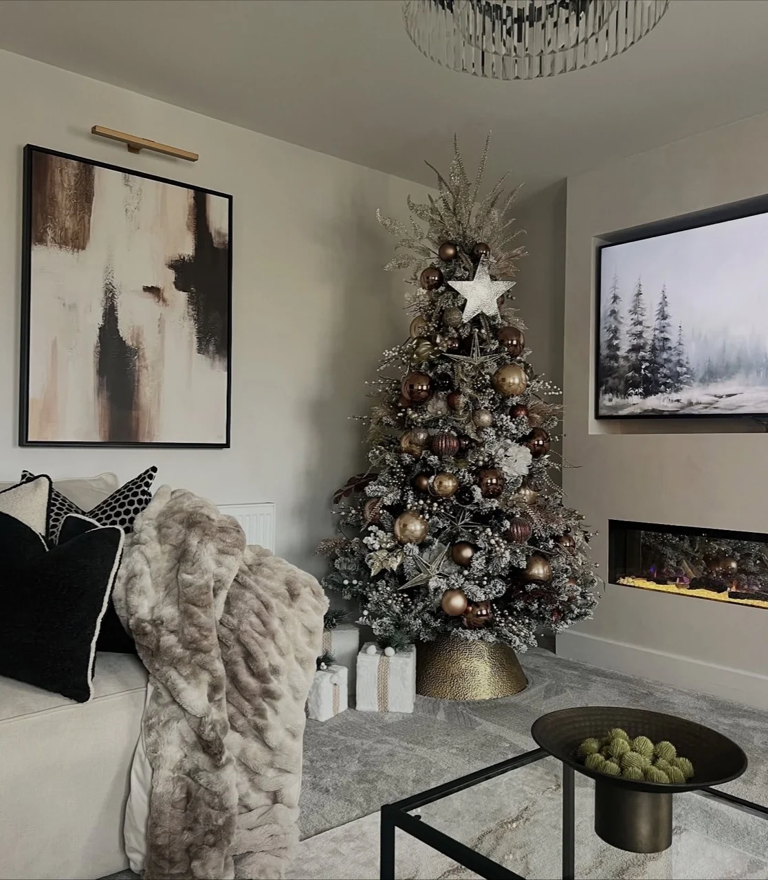 Flocked Christmas tree with bronze and gold baubles, white flowers and metallic foliage beside a cream sofa.